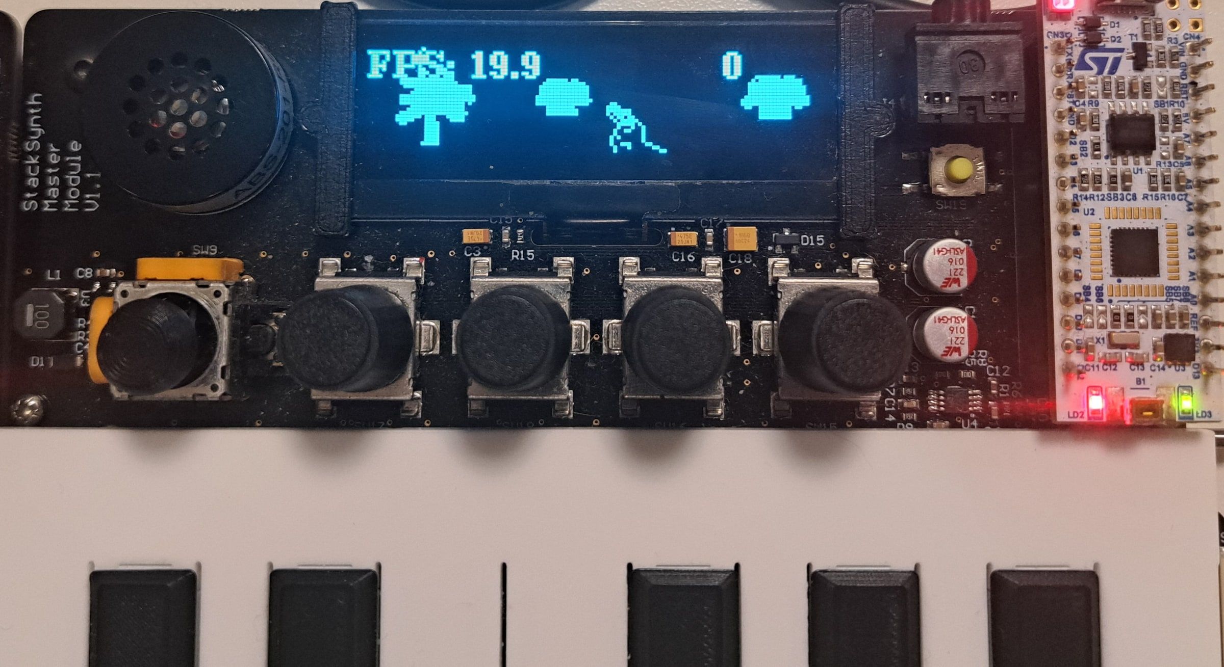 The synthesiser board with its OLED display showing the game: trees, an enemy and the player's gun, with an FPS counter reading 19.9.