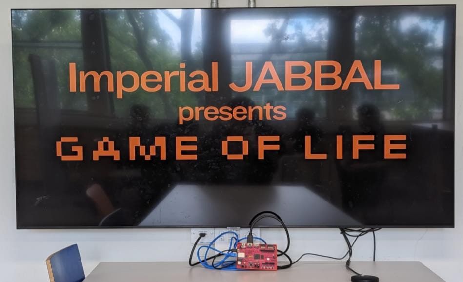 A large TV showing 'Imperial JABBAL presents GAME OF LIFE' in orange pixel lettering, with the red PYNQ-Z1 board on the table beneath it.